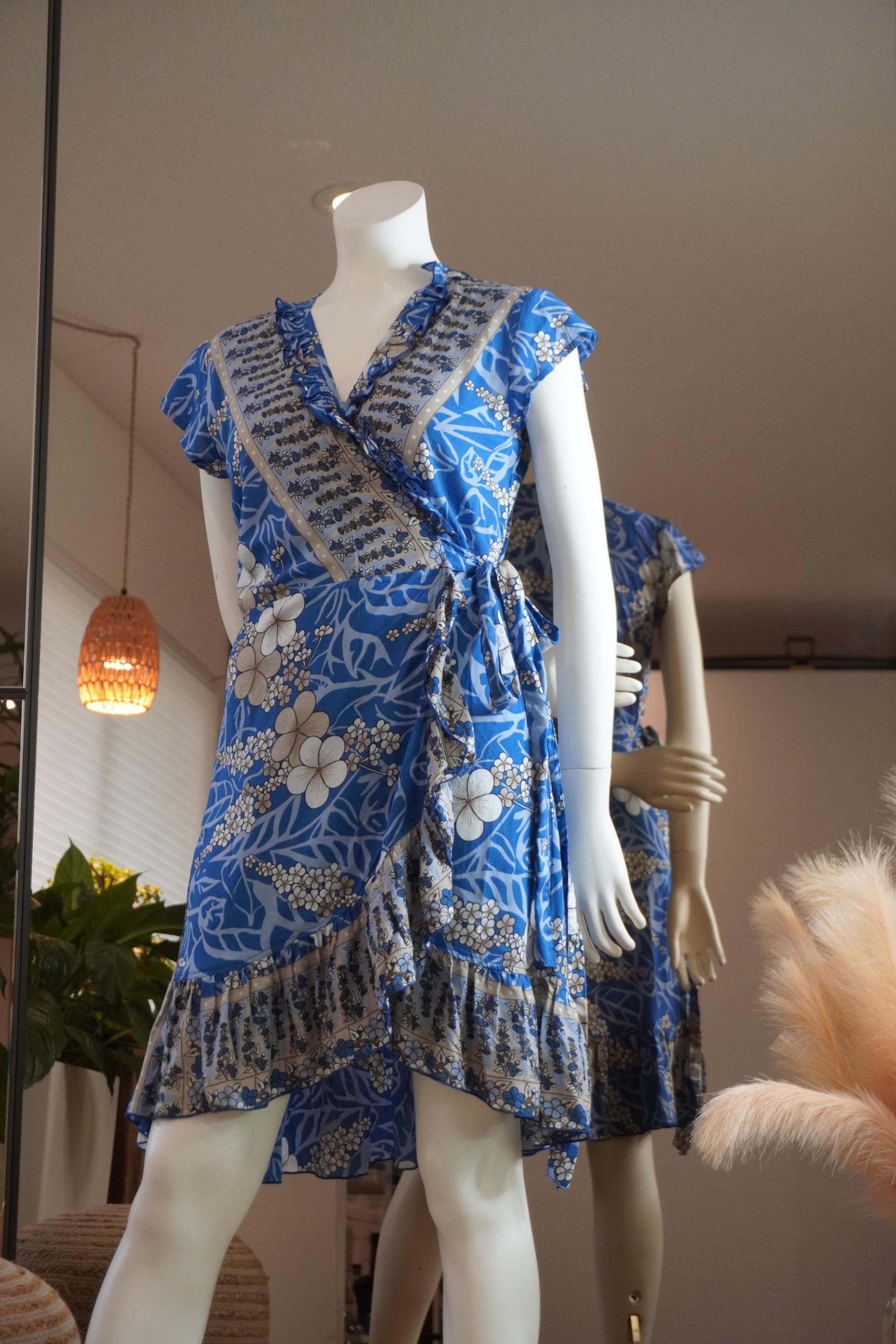 A mannequin wearing a blue wrap dress with a floral pattern and frills, displayed in a store.