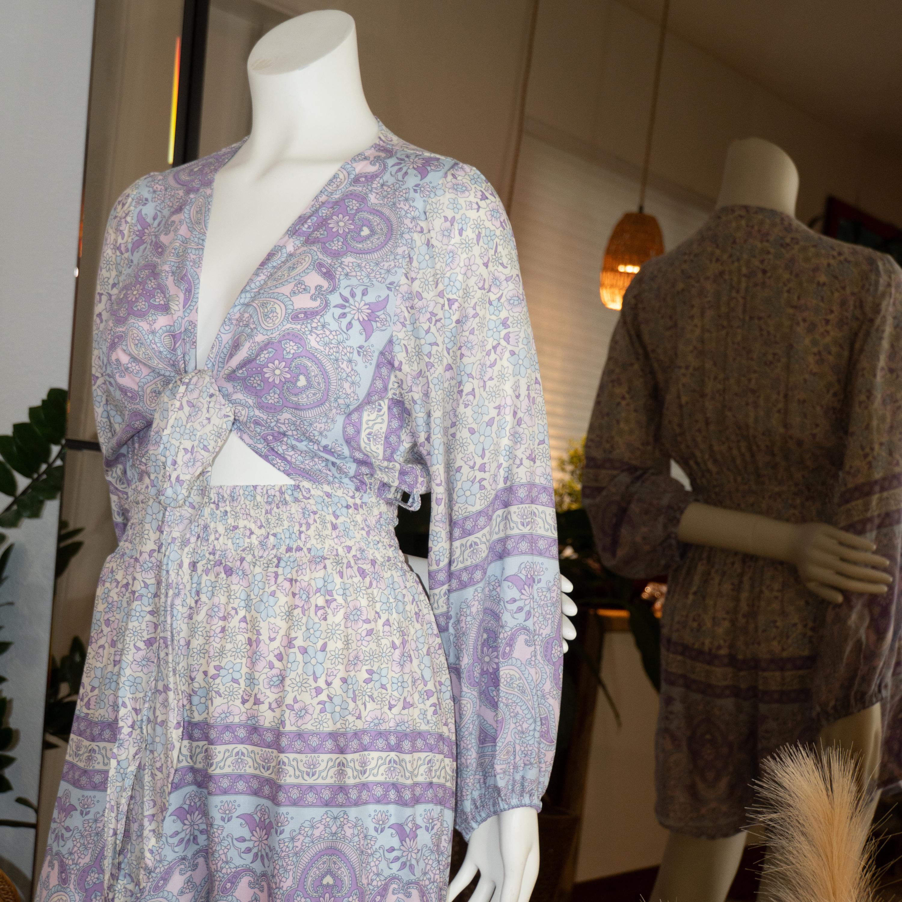 A mannequin wearing a purple and white patterned dress with a tie waist, displayed in a clothing store.