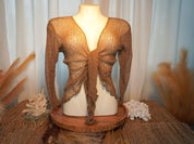 A mannequin wearing a brown, knitted top with a butterfly-like design, displayed on a wooden stand with coral and other natural elements.