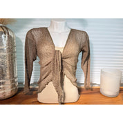A mannequin wearing a beige knitted cardigan with long sleeves, displayed on a wooden surface next to a glass vase and a candle.
