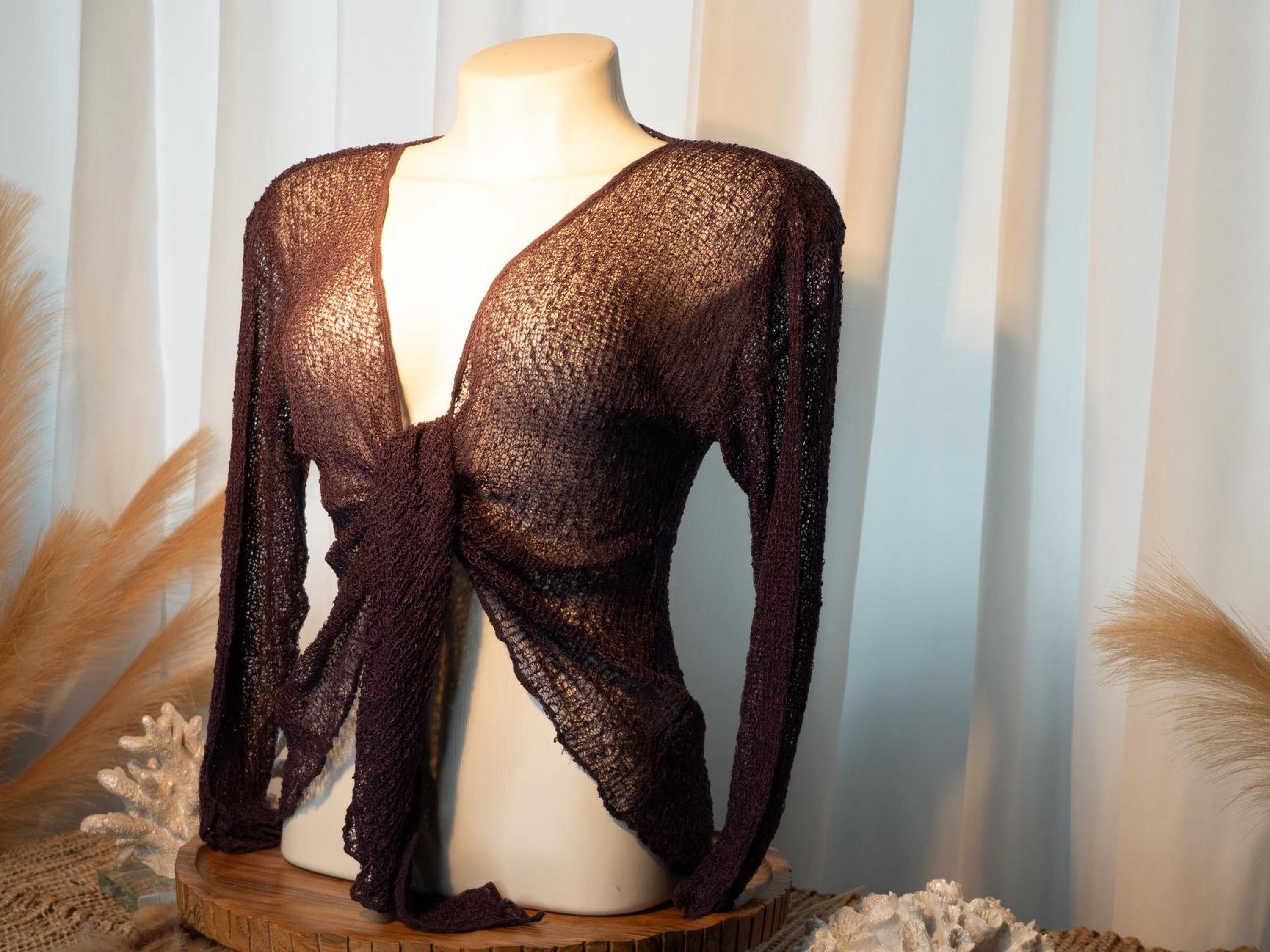A mannequin wearing a brown knitted top with long sleeves, displayed on a wooden stand against a white curtain background.
