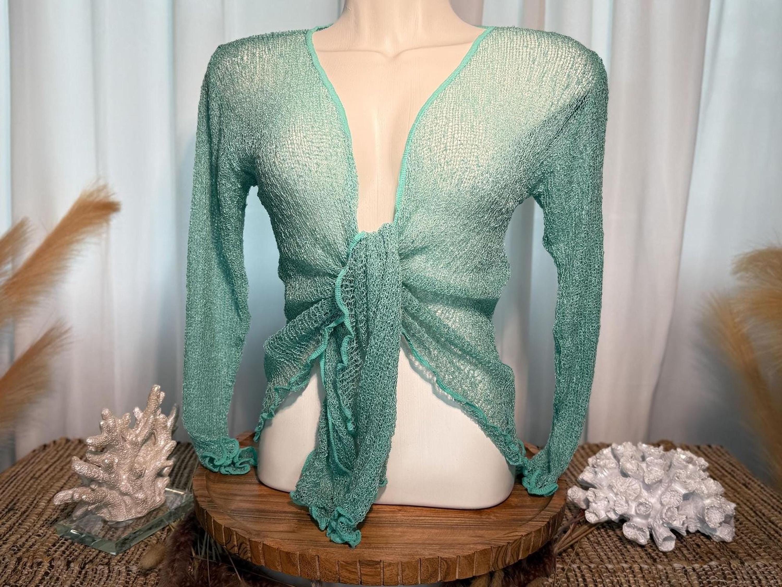 A mannequin wearing a mint green knotted top stands on a wooden stand, accompanied by a small white coral and a glass figurine.