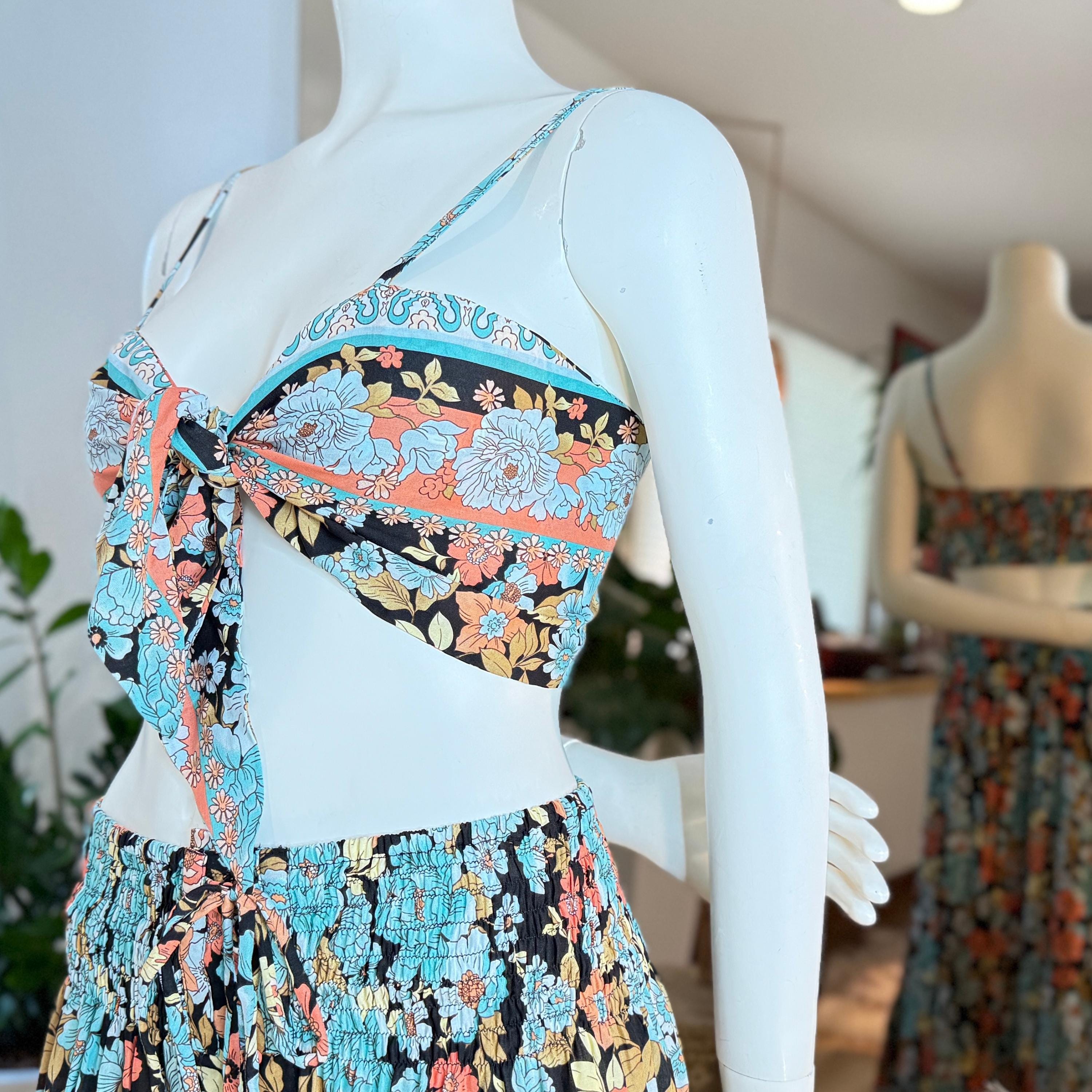 A mannequin wearing a colorful floral print dress with a tie waist and a matching skirt.