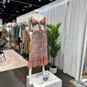 A mannequin wearing a colorful floral print dress and a matching crop top stands in a clothing store, surrounded by various clothing items on display.