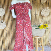 A mannequin wearing a red floral print dress with off-the-shoulder sleeves, placed in front of a bamboo wall with a woven basket containing yellow flowers.