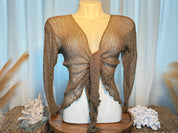 A mannequin wearing a brown, tie-front top with long sleeves, displayed on a wooden stand with a blue curtain backdrop.