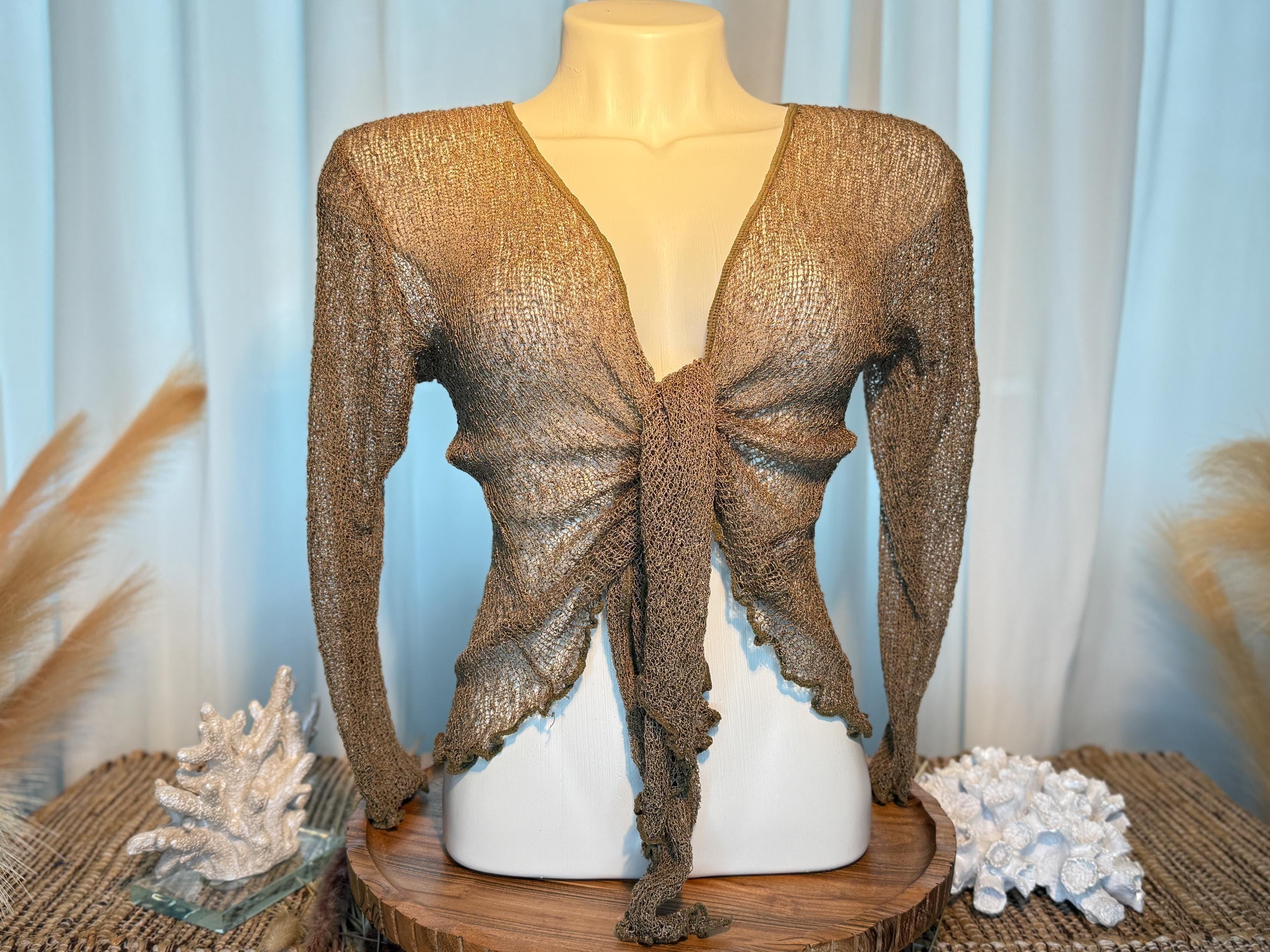A mannequin wearing a brown, tie-front top with long sleeves, displayed on a wooden stand with a blue curtain backdrop.