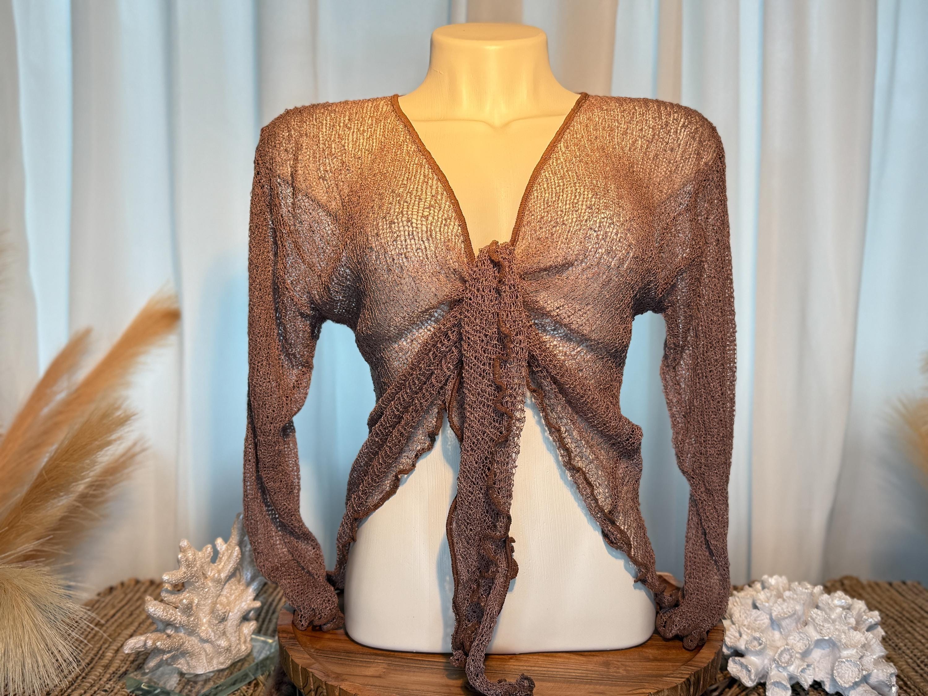 A mannequin wearing a brown knitted top with a tie front, displayed on a wooden stand with coral and other decorative items.