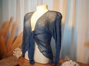 A mannequin wearing a blue knitted top with long sleeves, displayed on a wooden stand with coral and other natural elements in the background.