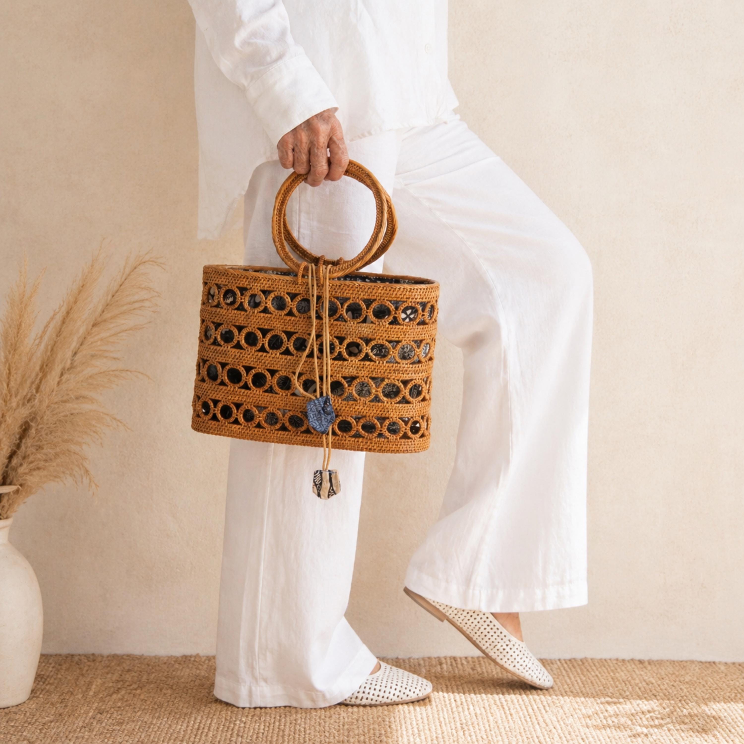 A person wearing white pants and shoes is holding a woven handbag with a distinctive pattern.