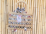 A woven handbag with a round handle and a tag displaying the text "CD Crafts Live Love" is displayed against a bamboo wall.