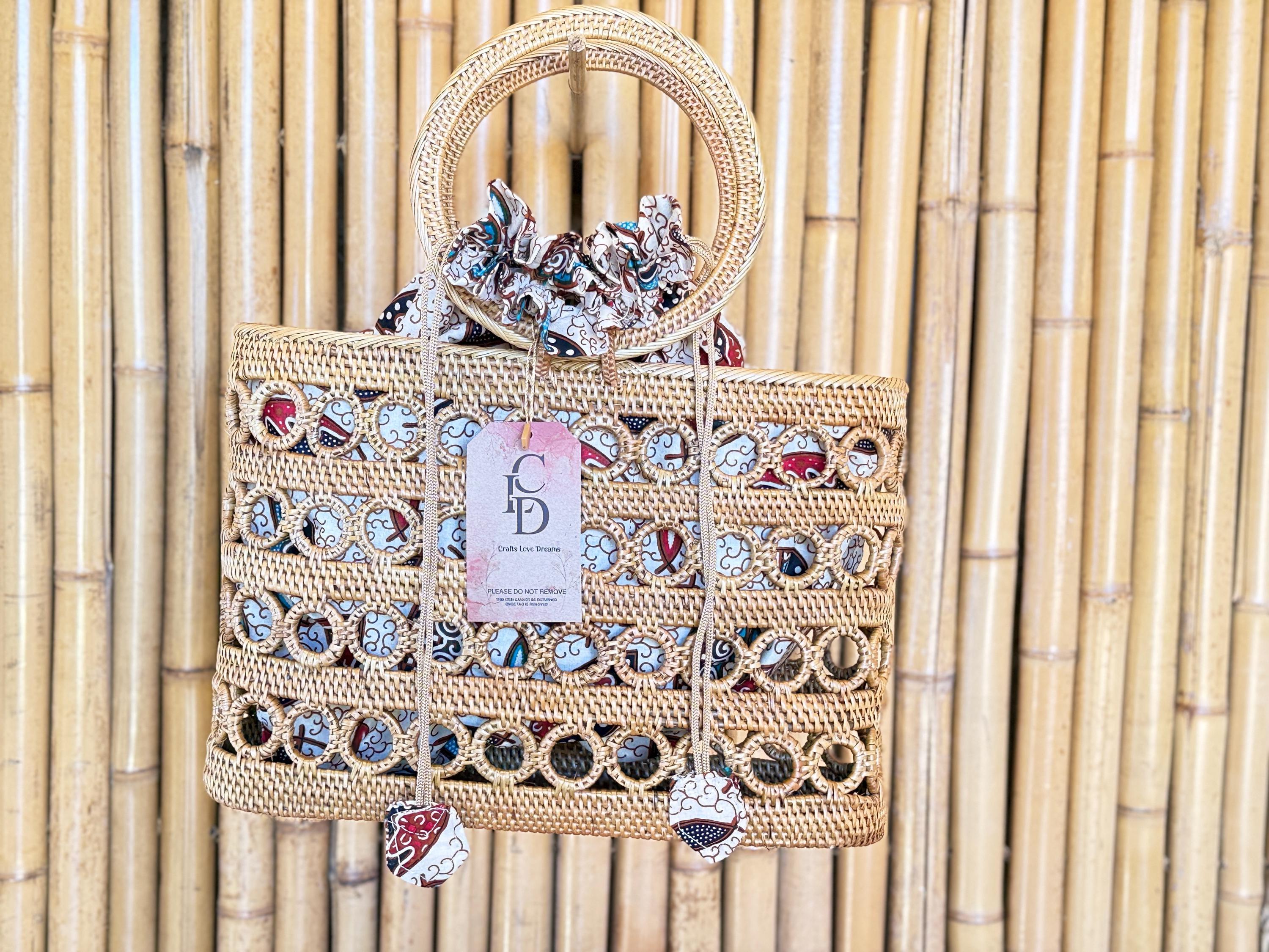 A woven handbag with a round handle and a tag displaying the text "CD Crafts Live Love" is displayed against a bamboo wall.