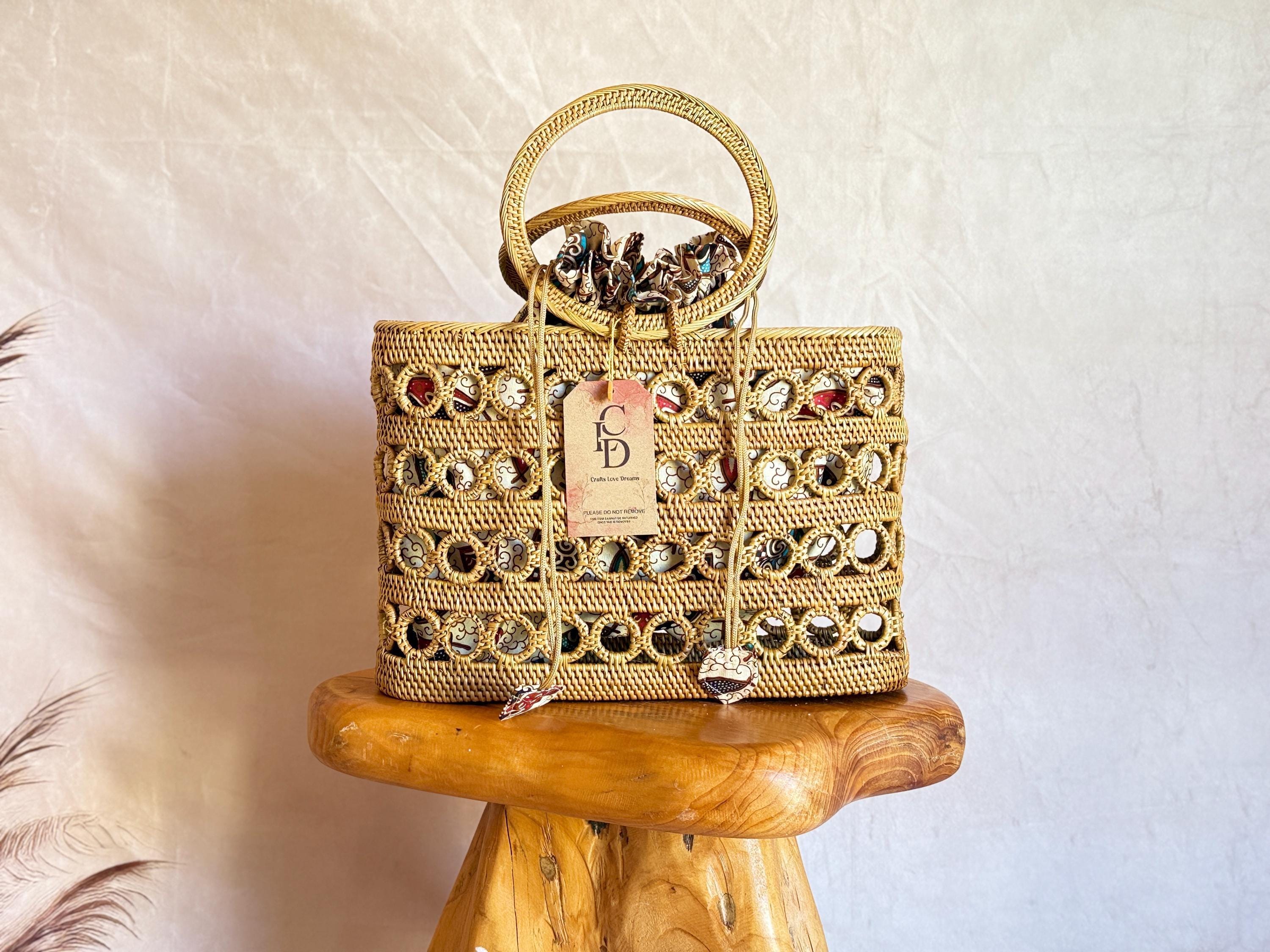A woven straw handbag with a handle and a tag, placed on a wooden stool against a plain background.