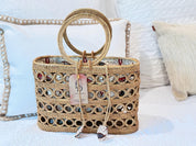 A woven handbag with a round handle and a tag attached, placed on a white bedspread.