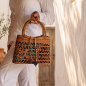 A person wearing white clothing is holding a woven purse with a distinctive pattern.