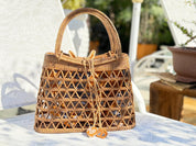 A woven straw handbag with a distinctive pattern sits on a white chair, with a potted plant visible in the background.
