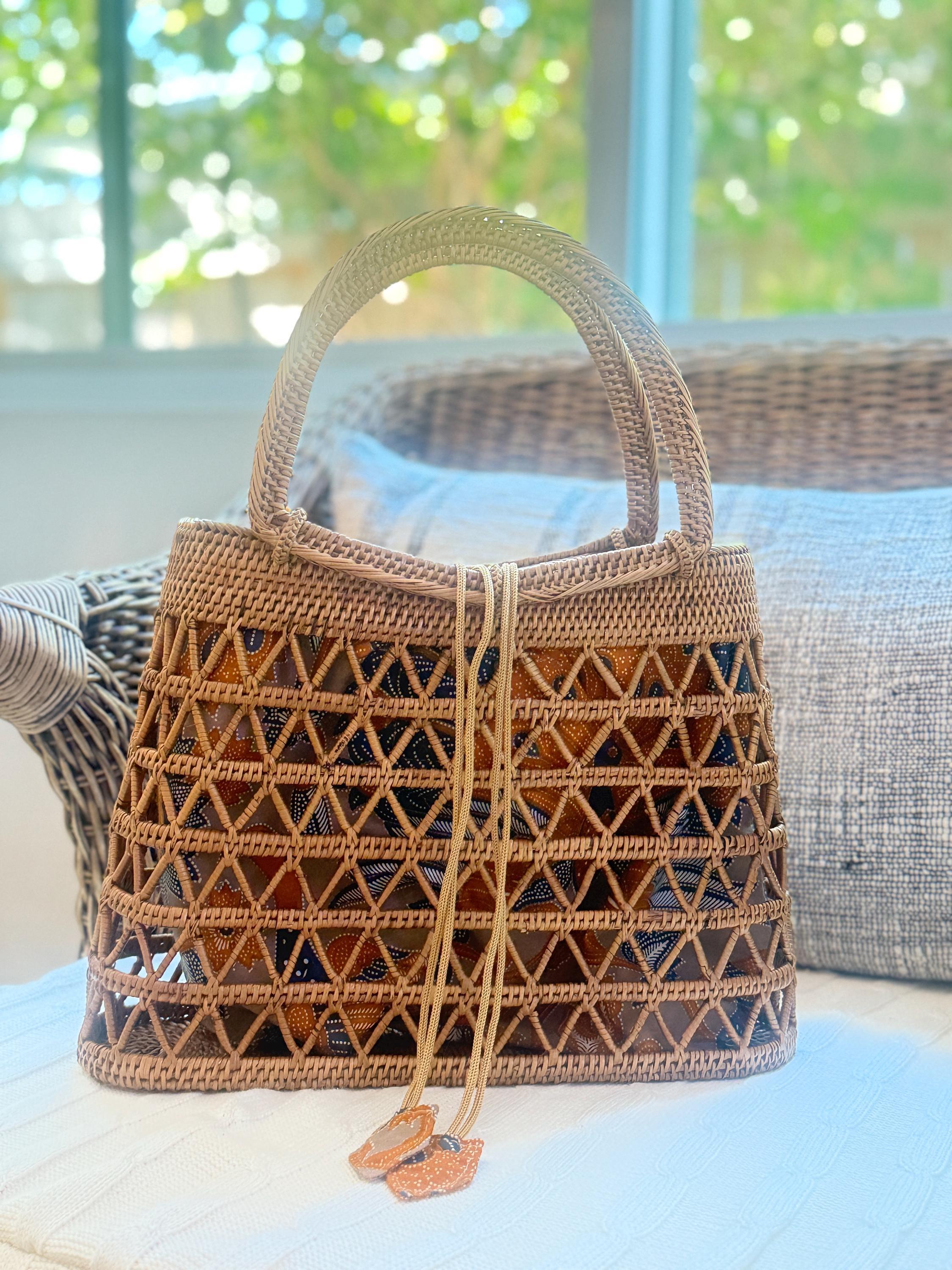 A woven handbag with a geometric pattern sits on a white surface, with a window and wicker furniture visible in the background.