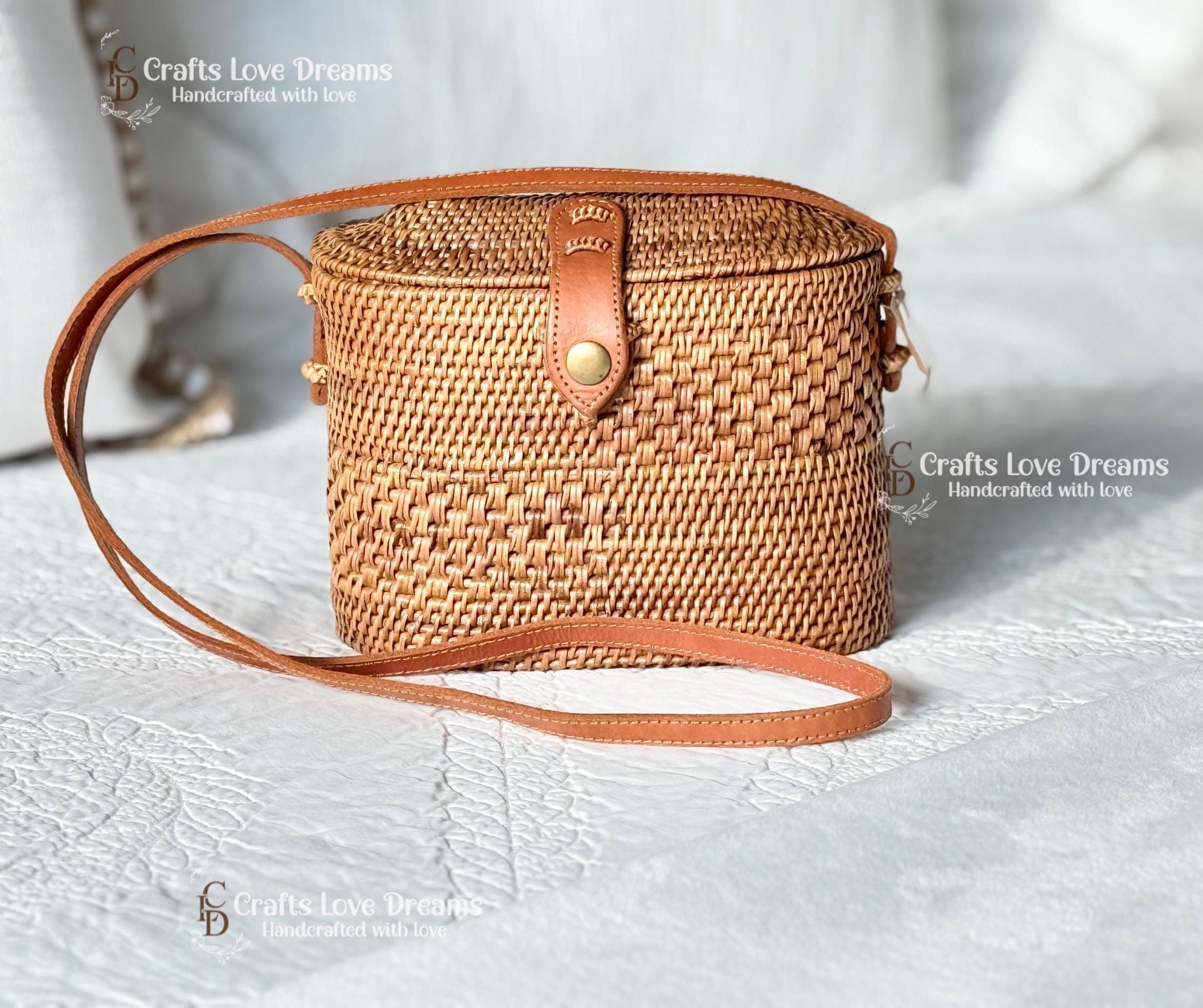 A woven straw bag with a leather strap, displayed on a white surface.