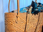 A woven straw bag with a patterned fabric draped over it, placed against a blue background.