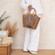 A person wearing white clothing and holding a woven handbag stands in a room with a wicker basket and some plants.