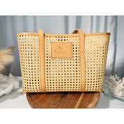 A tan woven tote bag with a leather-like texture, placed on a wooden surface against a blue background.
