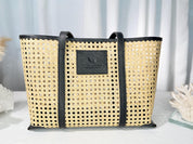 A woven tote bag with a black leather label, placed on a white surface against a blue background.