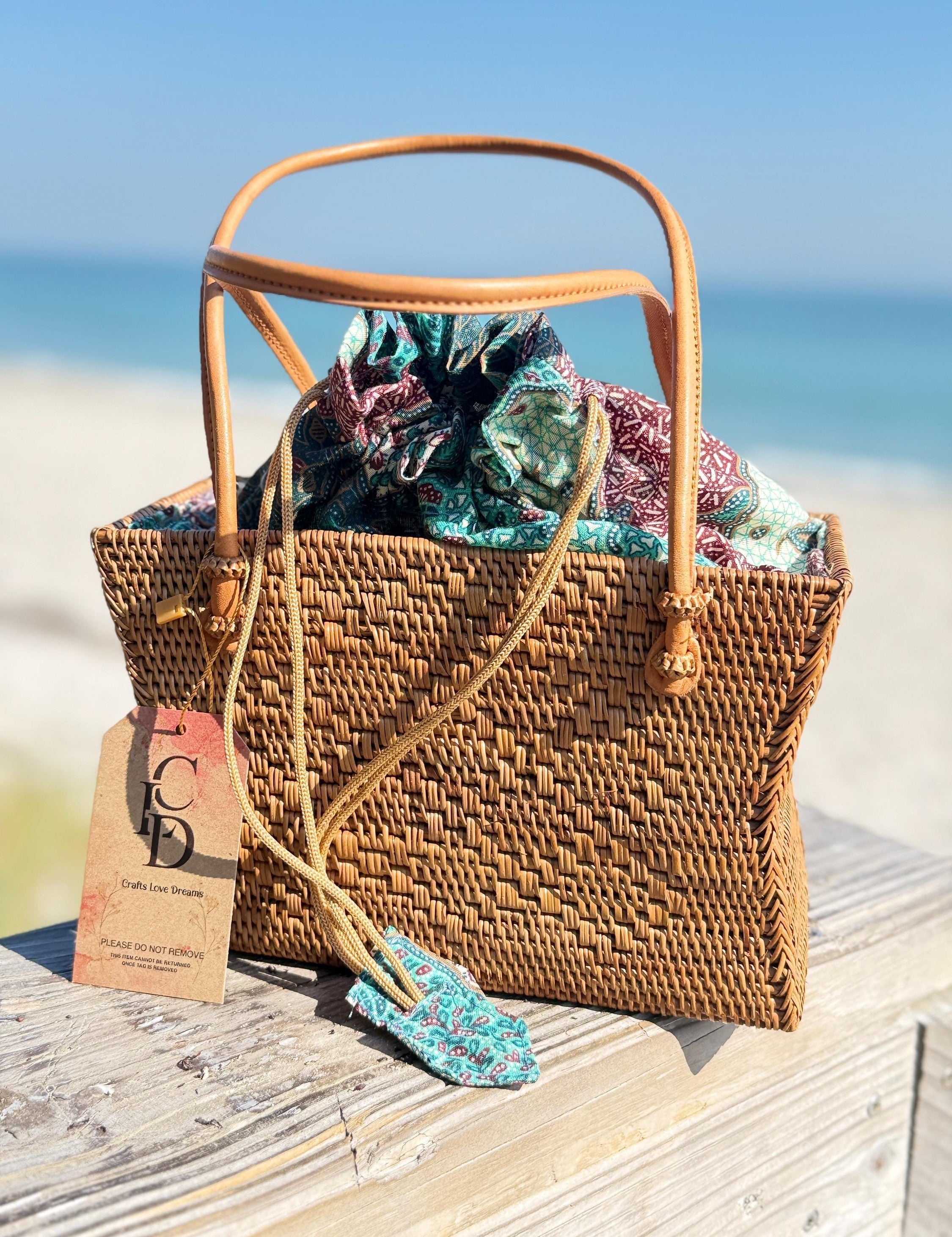A woven straw handbag with a floral pattern sits on a wooden surface, with a tag attached to it.