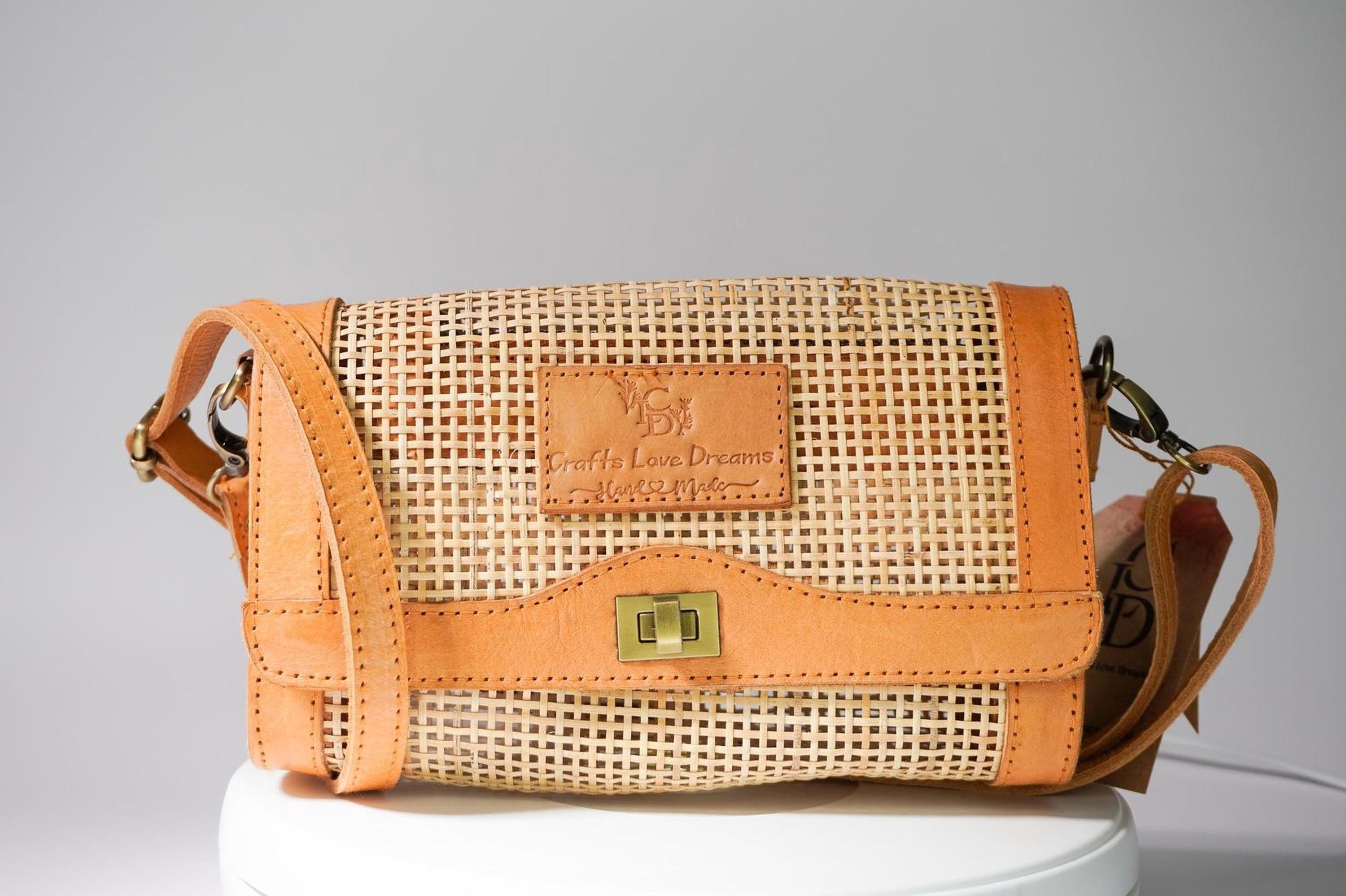 A tan-colored woven purse with a gold-colored clasp and a small leather patch on the front, sitting on a white surface.