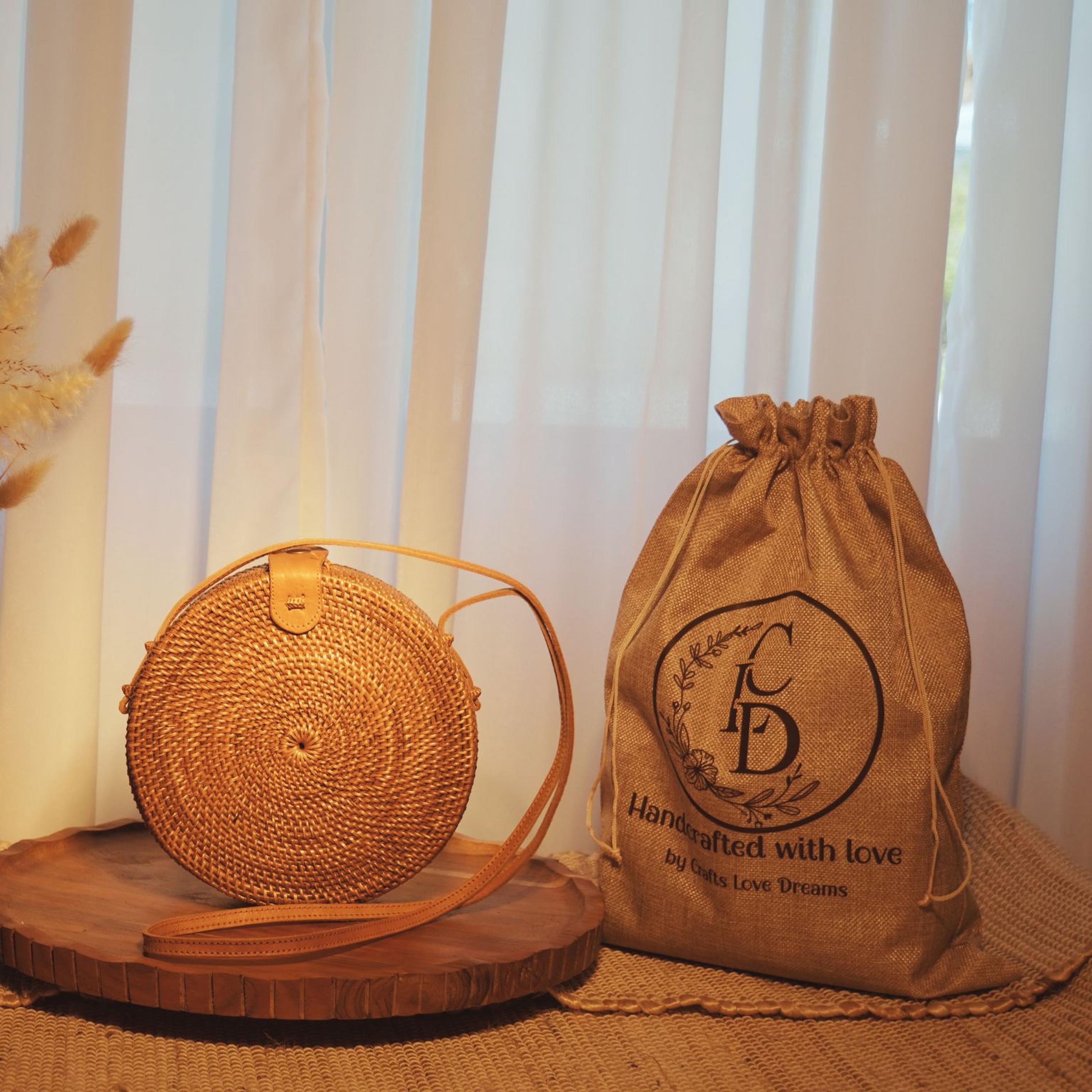 a round woven bag and a burlap sack with a logo, both placed on a wooden surface.
