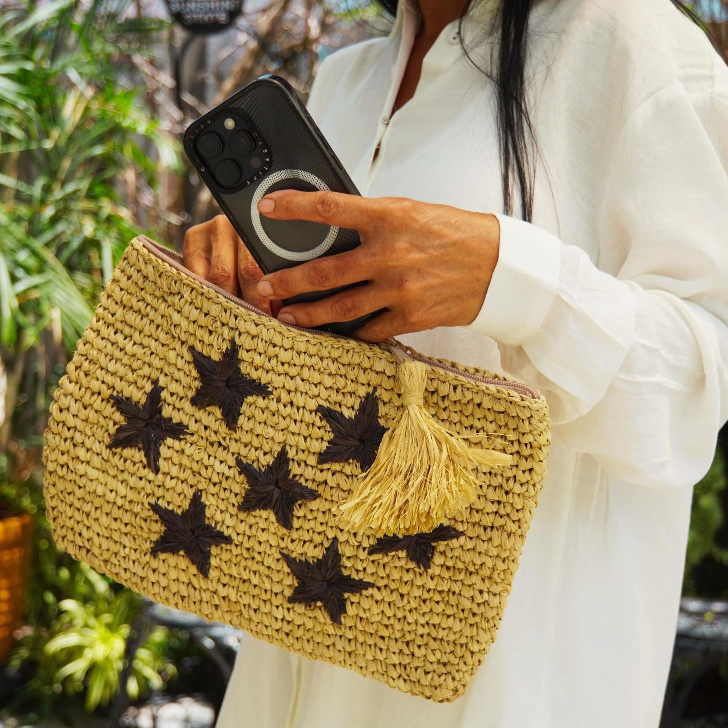 A person is holding a woven bag with star-shaped embellishments, and they are also holding a smartphone.