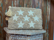 A woven purse with white star-shaped embellishments sits on a wooden surface against a rustic background.