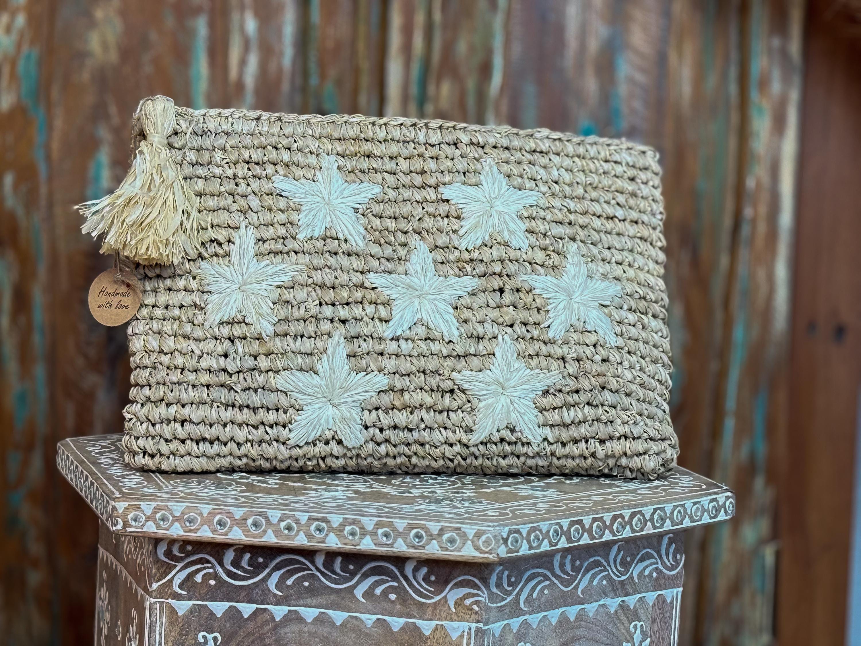 A woven purse with white star-shaped embellishments sits on a wooden surface against a rustic background.
