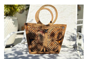 A woven handbag with a butterfly pattern sits on a white chair, with a tag attached to it.