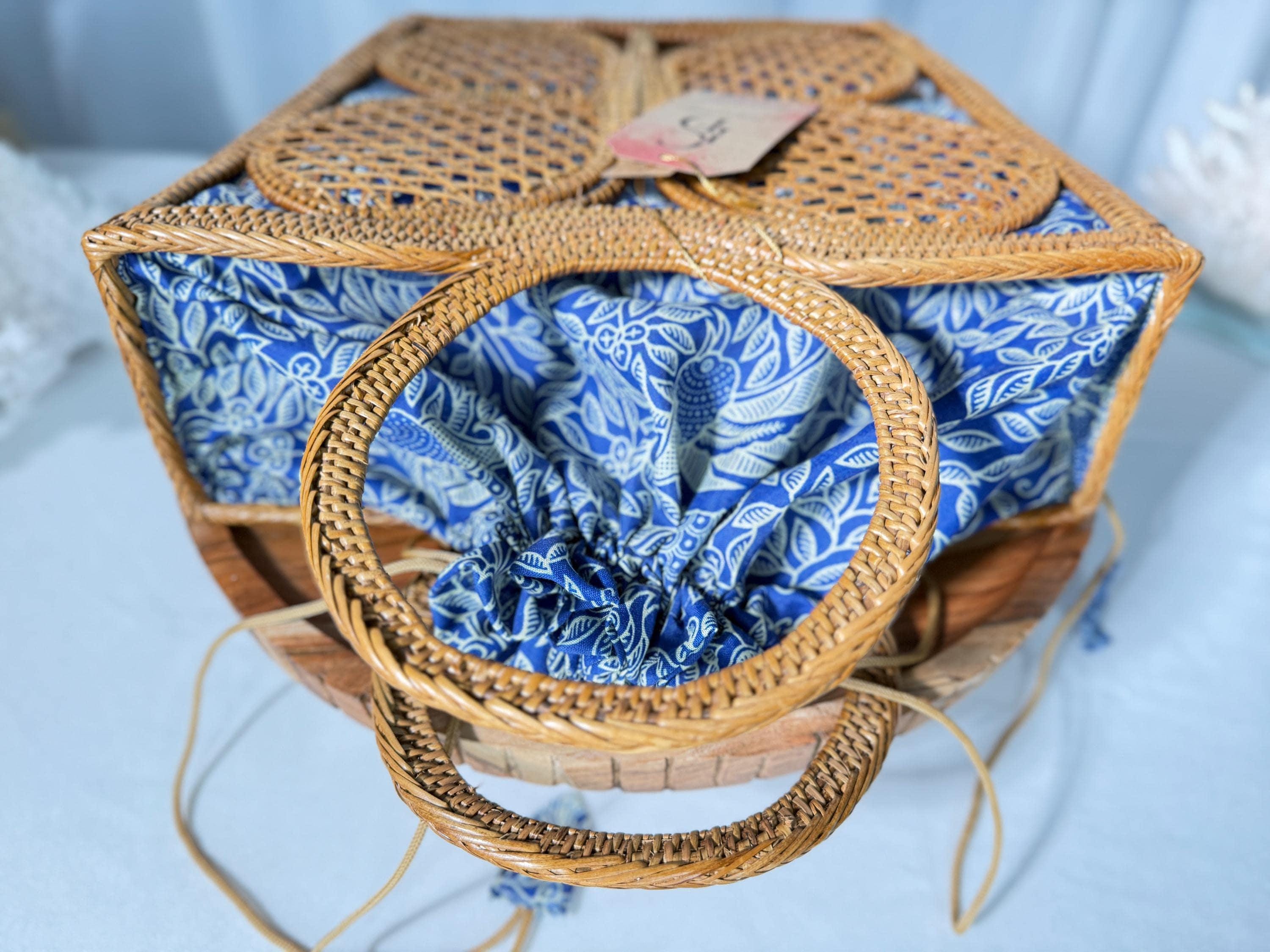 A woven basket with a blue and white floral pattern, featuring a handle and a small tag attached to it.