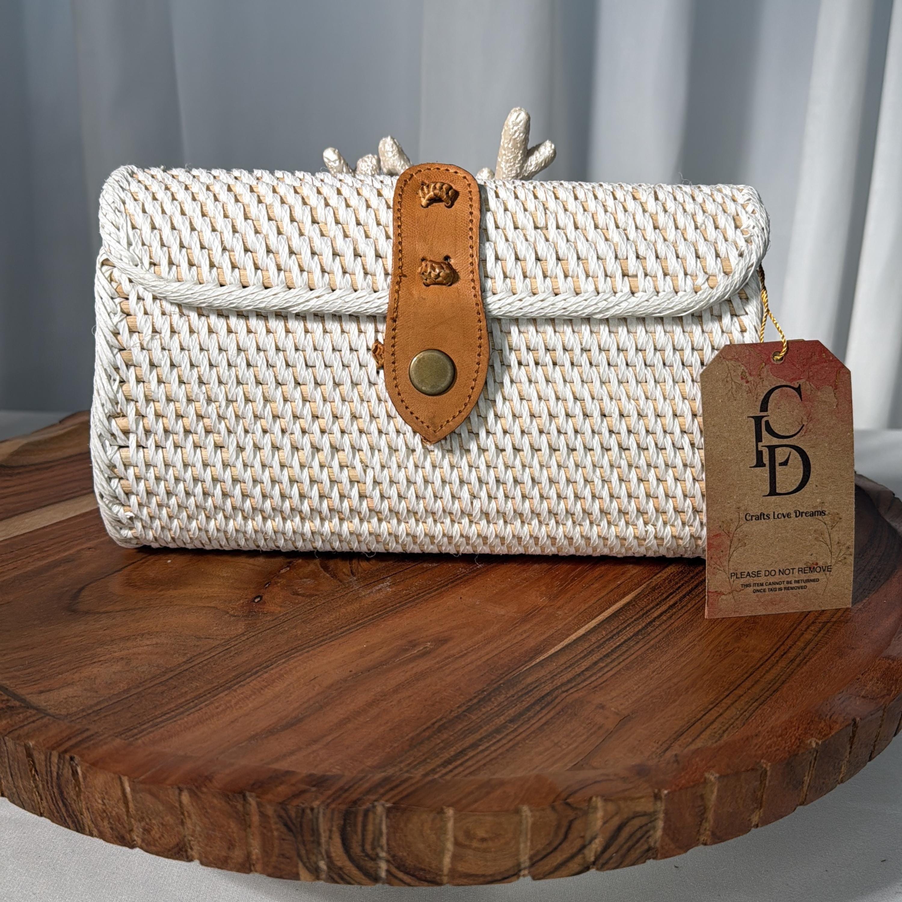 A white woven purse with a leather strap and a tag that reads "Crafts Love Dreams" is displayed on a wooden surface.