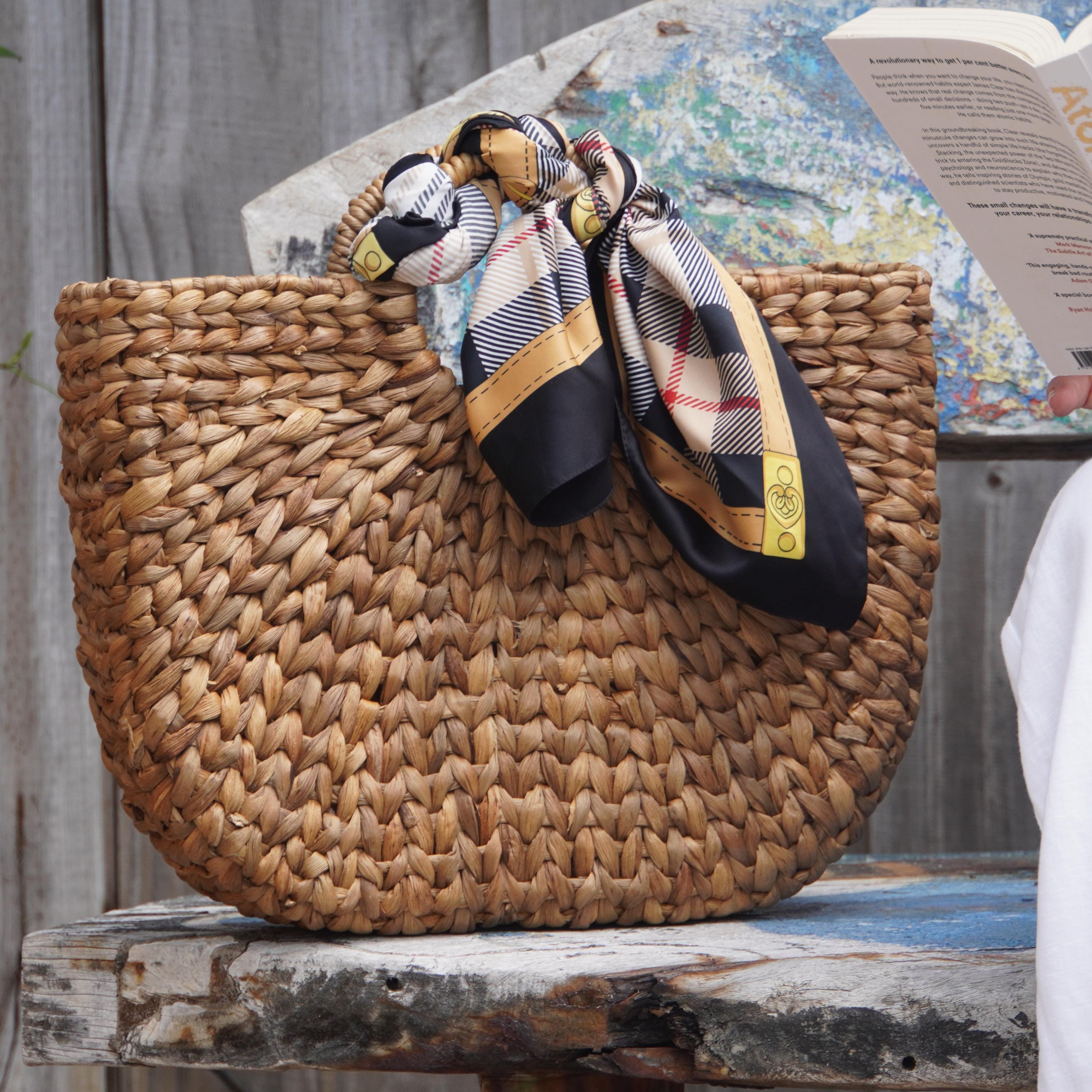 A woven straw bag with a plaid scarf tied around it, placed on a wooden surface.