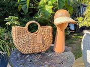 a woven straw handbag and a straw hat placed on a decorative metal table, surrounded by lush greenery.