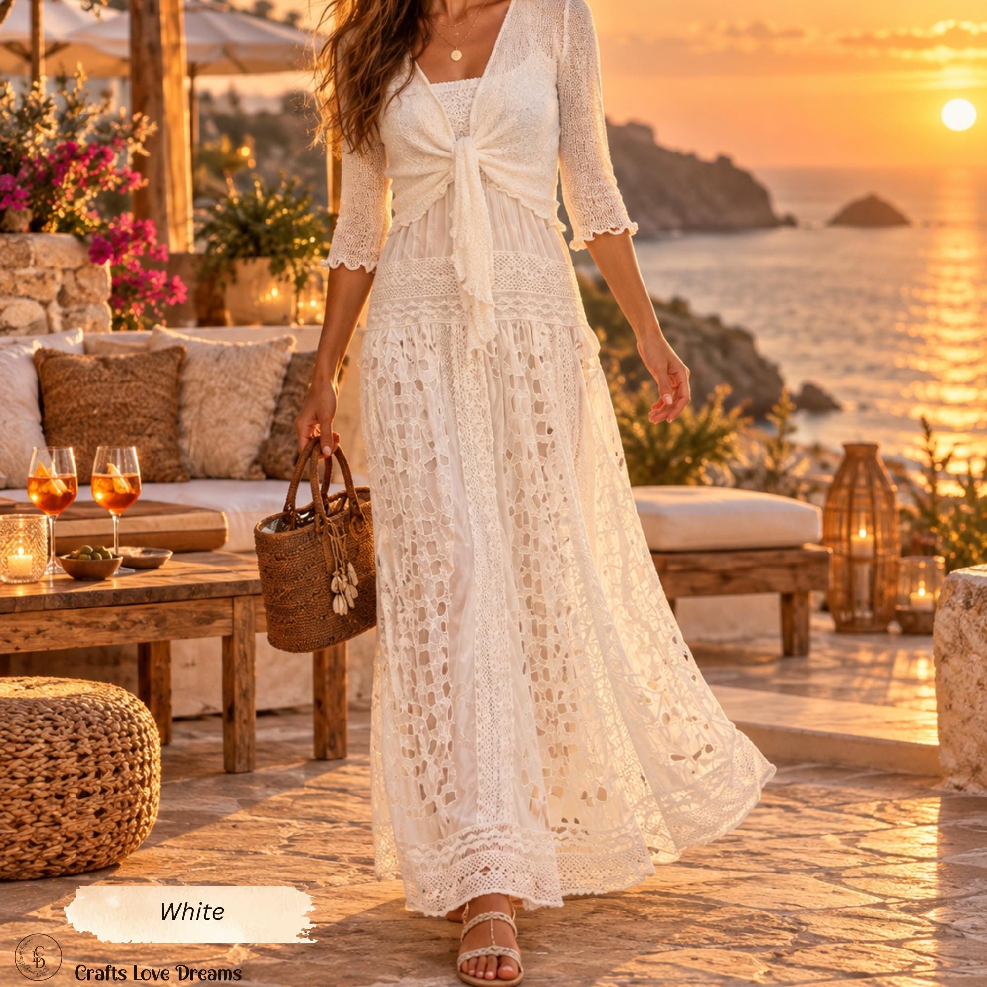 Woman in a white lace dress and off-white sheer knit cardigan shrug on a patio overlooking the ocean at sunset
